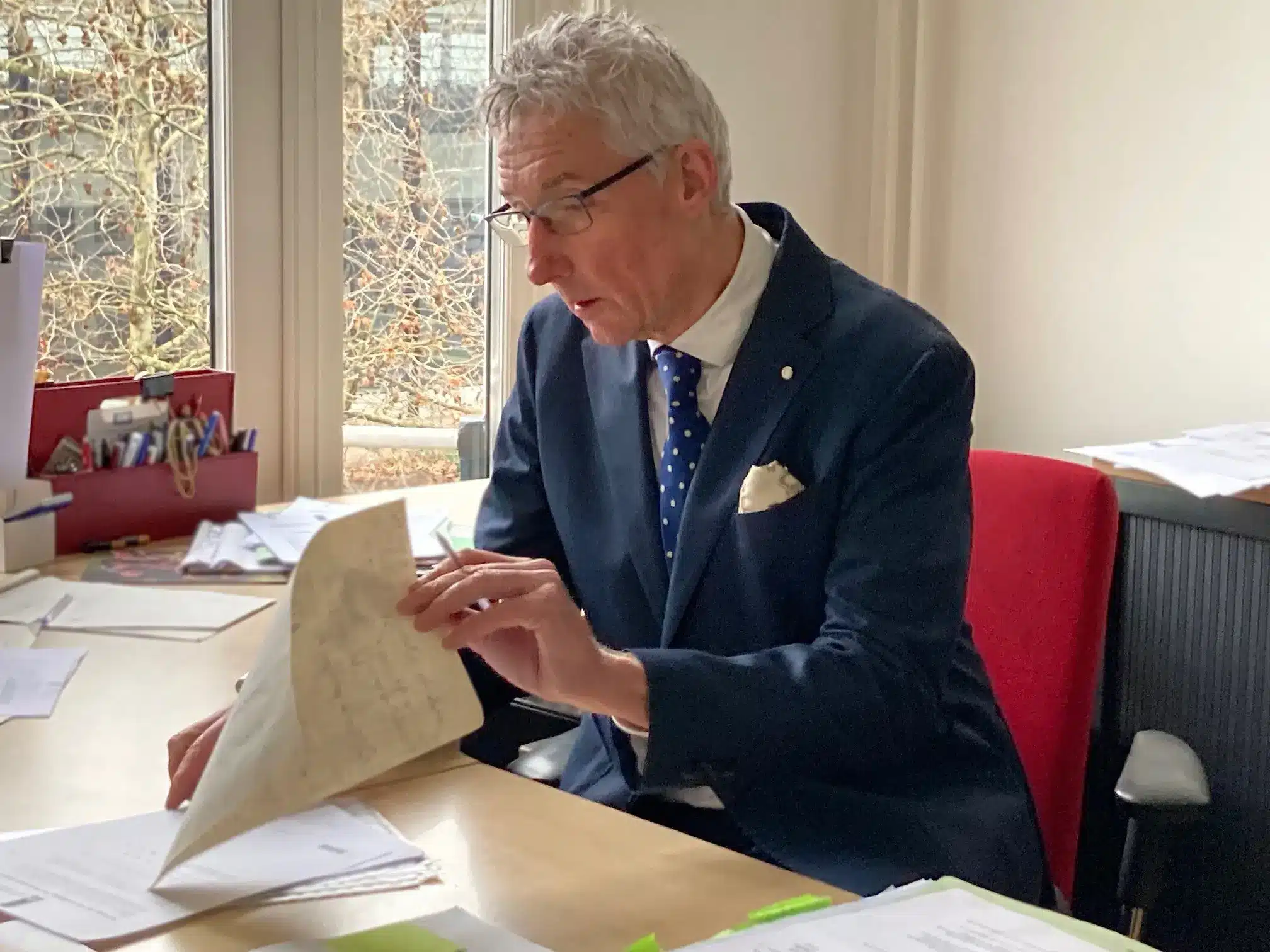 John Koreman aan zijn bureau met een document in zijn hand